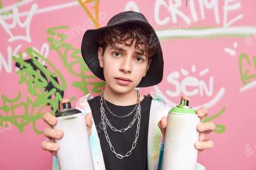 Preview: Youth Art Creativity Concept. Serious Curly Haired Hipster Wears Hat Shirt Metal Chains Around Neck