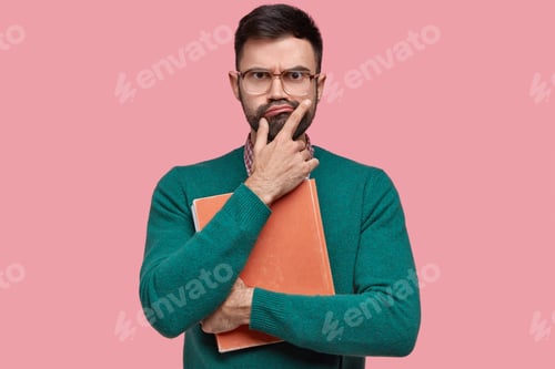 Preview: Displeased Unshaven Young Man Holds Chin, Purses Lips, Has Serious Unhappy Facial Expression, Holds