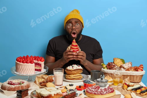Preview: Horizontal Shot Of Unshaven Man Holds Croissant, Has Stupefied Face Expression, Shock To Have Sugar