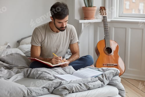 Preview: Dark Haired Young Man In T Shirt, Writes Information From Book Into Notebook, Sits Crosed Legs On