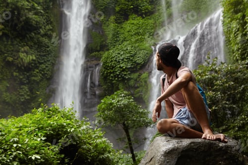 Preview: Travel And Adventure. Fashionable Young Man Wearing Snapback And Backpack Sitting On Stone And