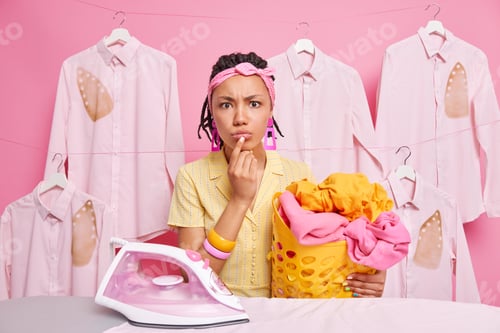 Preview: Serious Attentive Dark Skinned Young Woman Holds Basket Full Of Washed Laundry Irons Linen Looks
