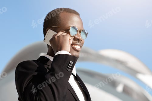 Preview: Happy Cheerful Black Businessman In Formal Wear And Sunglasses Talking On Smart Phone Outside