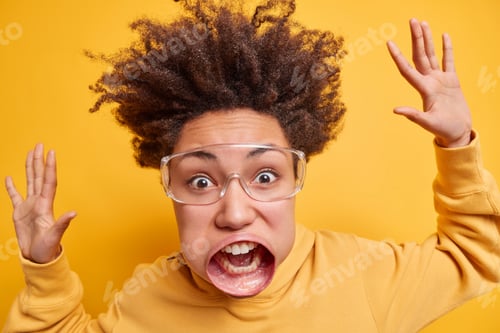 Preview: Close Up Portrait Of Emotional Curly Haired Woman Stares At Camera Has Very Huge Mouth Raises Arms