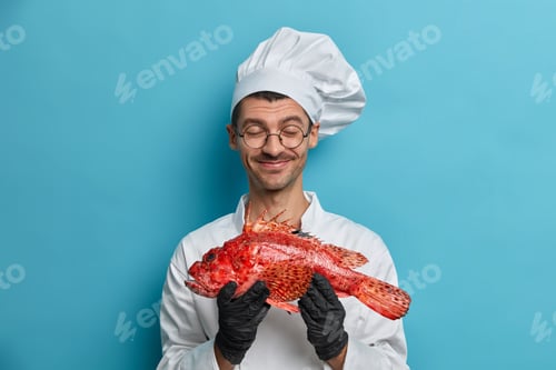 Preview: Shot Of Happy Male Cook In White Uniform Holds Raw Sea Bass In Hands Develops Restaurant Menu Cooks