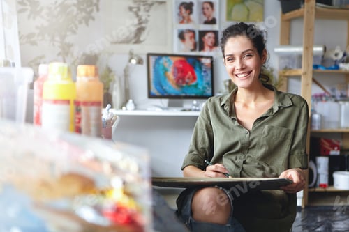 Preview: Smiling Female Artist Wearing Casual Clothes Sitting In Her Cabinet With Sketches And Colorful