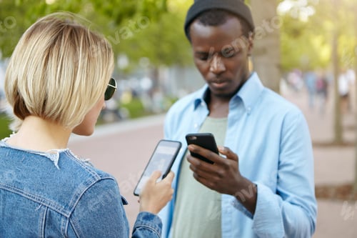 Preview: Fashionable Dark-Skinned Male In Black Hat And Shirt Standing On Street With Mobile Phone And His