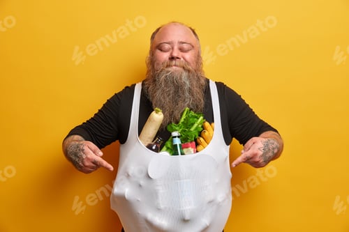 Preview: Pleased Delighted Bearded Man Points At Stomach Full With Products, Has Addiction To Food, Stands