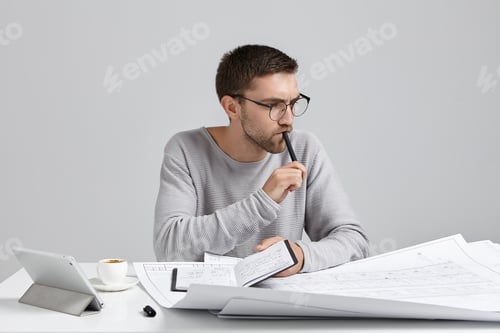 Vista previa: Un ingeniero serio y pensativo guarda el bolígrafo y el cuaderno en la mano, planifica reuniones, mira dibujos y