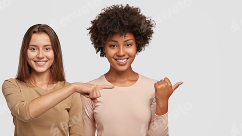 Preview: Photo Of Satisfied Interracial Young Women Point Aside With Joyful Expressions, Show Nice Place To