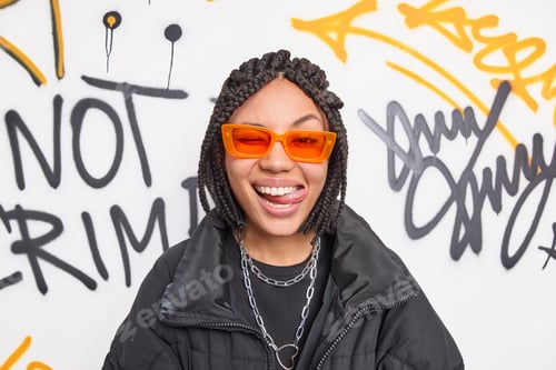 Preview: Cheerful Fancy Teenage Girl Wears Trendy Orange Suglasses And Black Jacket Sticks Out Tongue Has