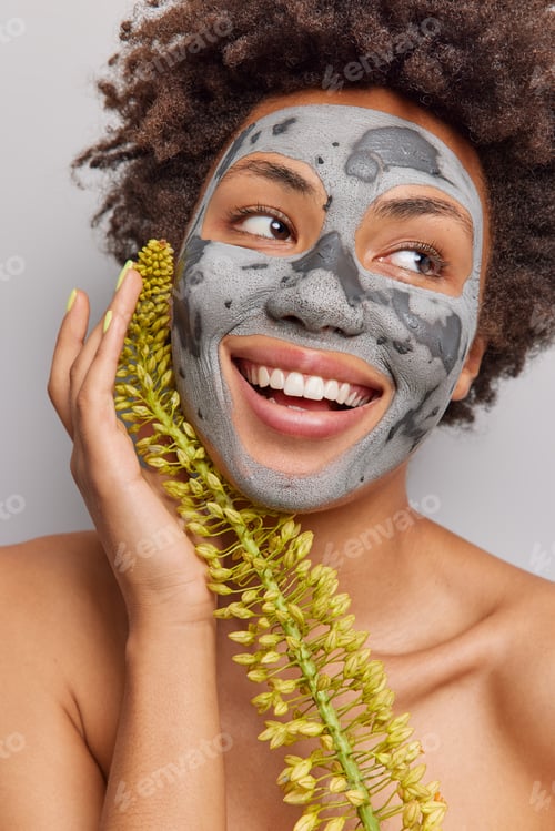 Preview: Woman with clay mask smiling and holding flower