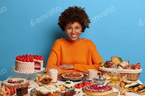 Preview: Desserts, Fast Food, Unhealthy Lifestyle Concept. Pleased Dark Skinned Model In Orange Jumper