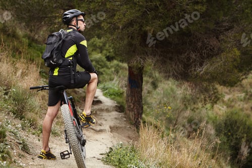 Preview: Outdoor Shot Of Young European Male Wearing Cycling Clothing, Helmet And Glasses Standing On Track