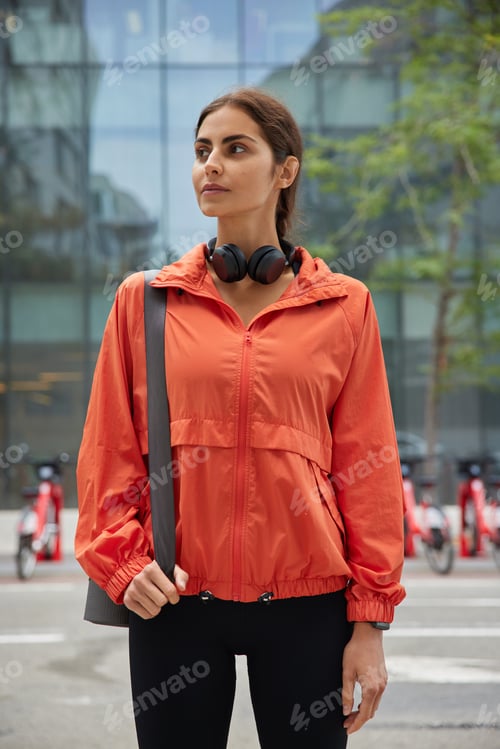 Preview: Vertical Shot Of Thoughtful Woman On Her Way To Outdoors Yoga Class Walks With Exercise Mat Wears