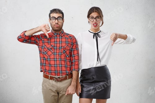 Preview: Studio Portrait Of Wonky Man And Woman Express Dislike, Disapproval Or Disregard, Keep Thumbs Down