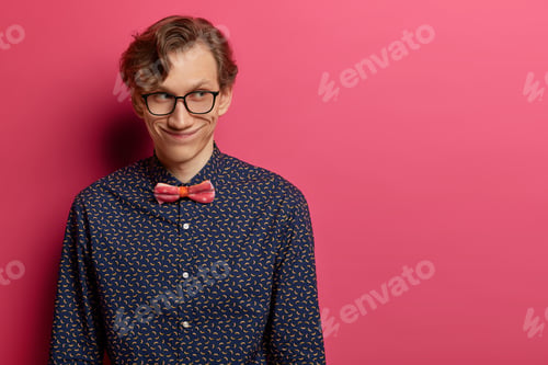 Preview: Mysterious Happy Adult Man Has Broad Smile On Face, Concentrated Aside, Stands Indoor Over Rosy