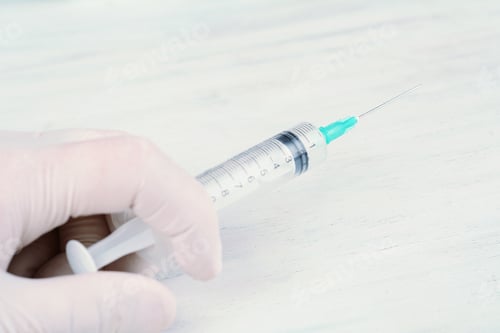 Preview: Doctor Hand With White Glove Holding Syringe Over White Wooden Background. Medicine Concept