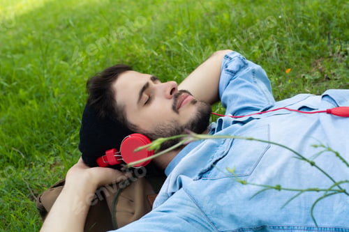 Preview: Young Man Relaxing On Green Grass With Headphones. Leisure Concept.