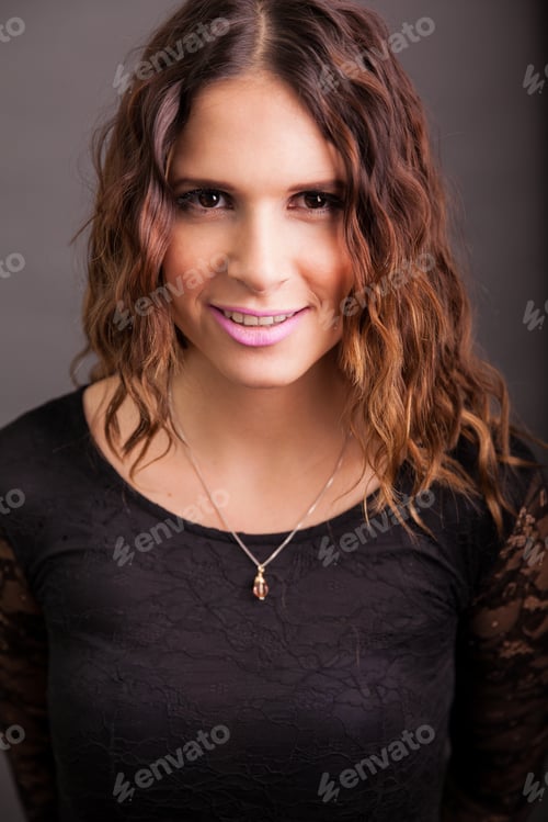Preview: Beautiful Young Brunette Wearing A Black Dress Against A Gray Background And Smiling