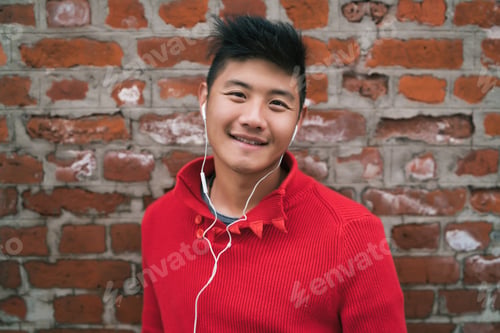 Preview: Portrait Of Young Asian Boy Listening To Music With Earphones Outdoors Against Brick Wall. Urban