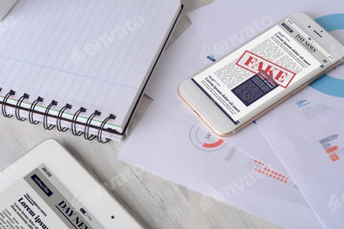 Preview: Close Up Of Spiral Notepad, Tablet, Financial Papers And Smartphone With Digital Fake News On