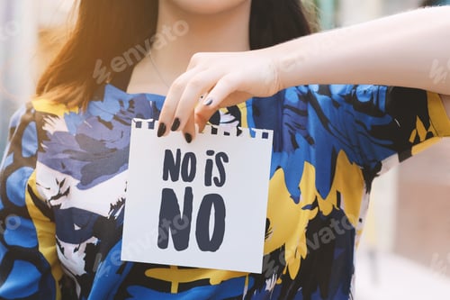 Preview: Closeup Of A Young Woman Outdoors Showing A Notepad With The Text "No Is No" Written In It.