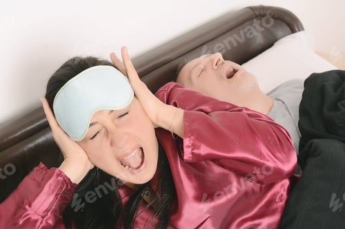 Preview: Portrait Of Irritated Woman Blocking Ears With Hands While Man Snoring On Bed. Indoors