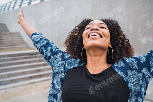 Preview: Portrait Of Young Afro American Woman Standing Outdoors With Arms Raised And Laughing.