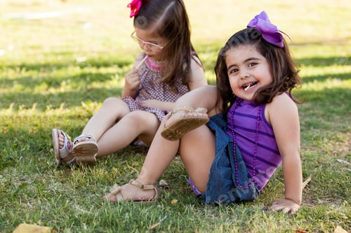Preview: Funny Little Girl Relaxing And Eating A Lollipop With A Friend At A Park