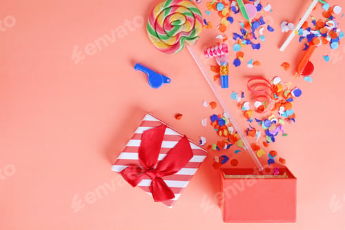 Preview: Red Gift Box With Party Confetti, Streamers And Noisemakers On Orange Background. Celebration