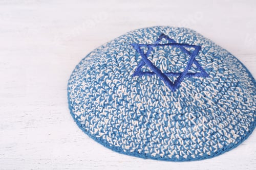 Preview: Knitted Kippah With Embroidered Blue Star Of David With Copy Space On A Wooden Table. Jewish