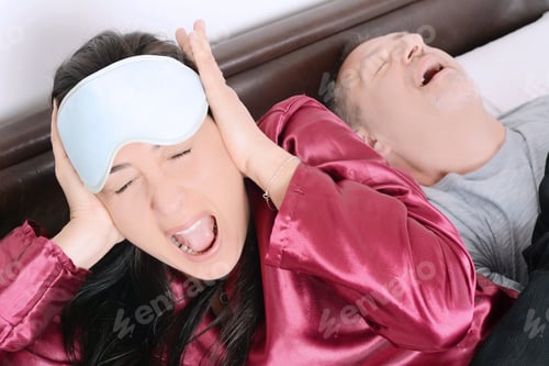 Preview: Portrait Of Irritated Woman Blocking Ears With Hands While Man Snoring On Bed. Indoors
