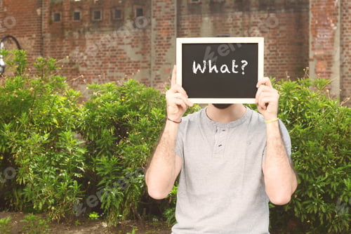 Preview: Portrait Of Handsome Young Man Holding Chalkboard With Text "What?". Outdoors.