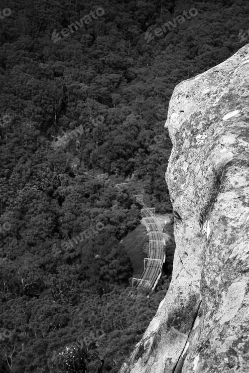 Preview: A Vertical Grayscale Shot Of A Rocky Mountain And A Bridge In The Middle Of A Forest