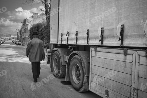 Preview: A Grayscale Shot Of A Male Wearing A Black Hat And A Coat Walking Down The Street