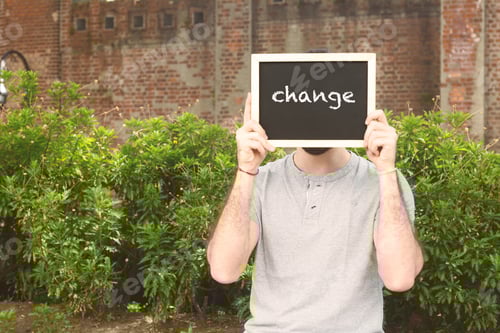Preview: Portrait Of Handsome Young Man Holding Chalkboard With Text "Change". Outdoors.
