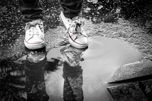 Preview: A Grayscale Shot Of A Man In White Sneakers Standing Near A Puddle