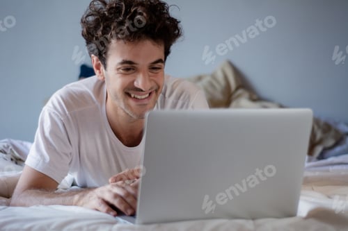 Preview: Happy Young Man Using Laptop And Relaxing On His Bed At Home. Indoors