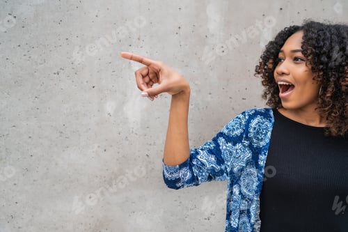 Preview: Portrait Of Beautiful Young Afro-American Woman With Curly Hair Pointing Something Against Grey