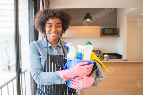 Preview: Portrait Of Young Afro Woman Holding A Bucket With Cleaning Items At Home. Housekeeping And