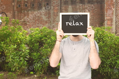 Preview: Portrait Of Handsome Young Man Holding Chalkboard With Text "Relax". Outdoors.