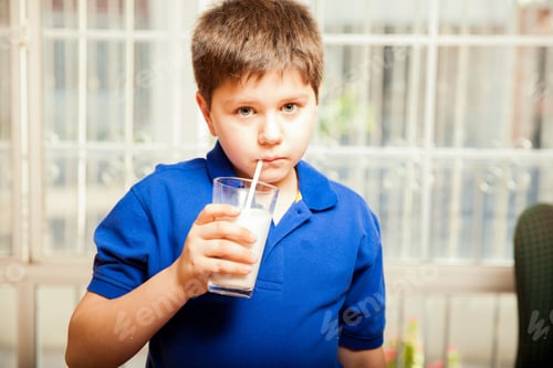 Preview: Blond Kid Drinking His Milk With A Straw At Home And Making Eye Contact