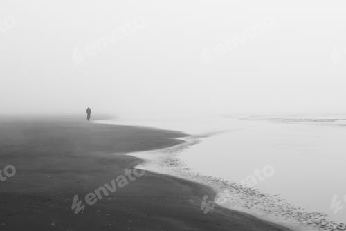 Preview: A Grayscale Shot Of A Lonely Person Walking On The Beach Under Dark Clouds