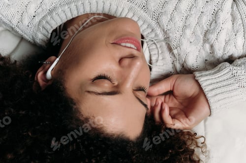 Preview: Portrait Of Young Latin Woman Wearing Earphones While Lying In Bed At Home. Girl Relaxing On Bed.