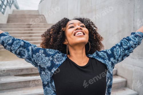 Preview: Portrait Of Young Afro American Woman Standing Outdoors With Arms Raised And Laughing.