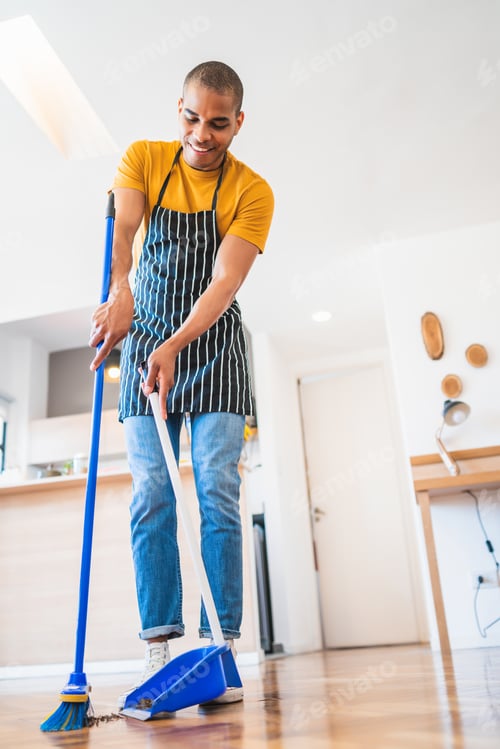 Preview: Portrait Of Young Latin Man Sweeping Wooden Floor With Broom At Home. Cleaning, Housework And