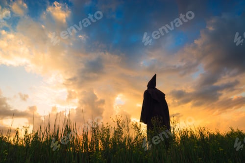 Preview: Silhouette Of Monk On A Hill Against Sky With Dramatic Colorful Clouds In A Light Of Sunset.