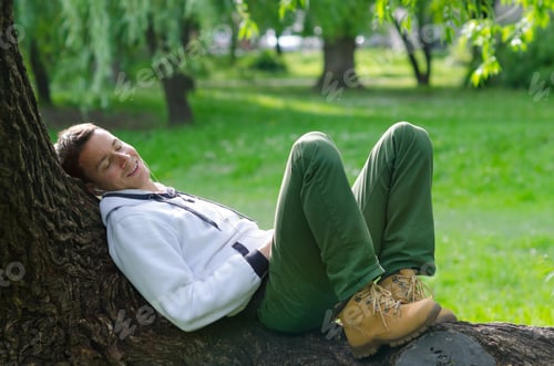 Preview: Young Man Listening Music On Mobile Phone In Park On Sunny Spring Day.