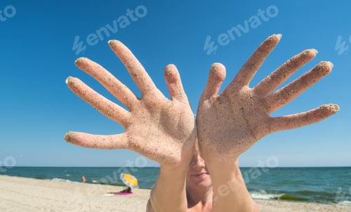 Preview: Woman Show'S Hands Covered With Sand On A Blue Sea Background.